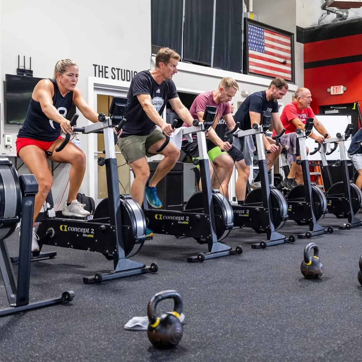 Cycle on stationary bikes in a gym with kettlebells.