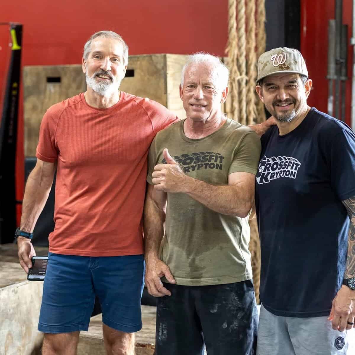 Athletes pose in a gym, one giving a thumbs-up.