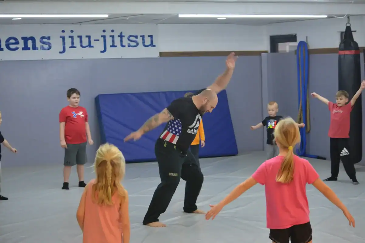 Wodify coach teaches kids jiu-jitsu, demonstrating a move in a gym.