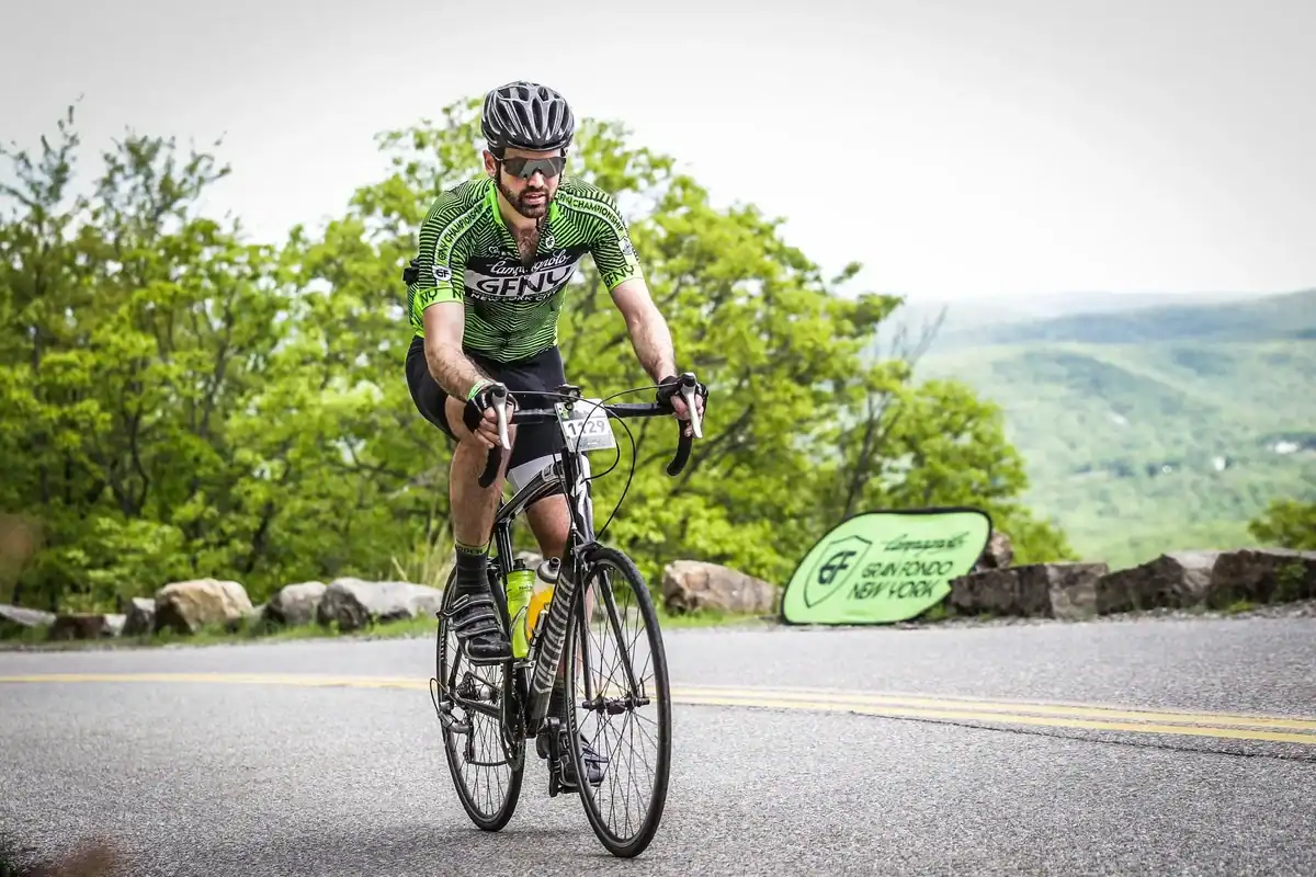 Athlete cycles uphill on a winding road surrounded by green trees.