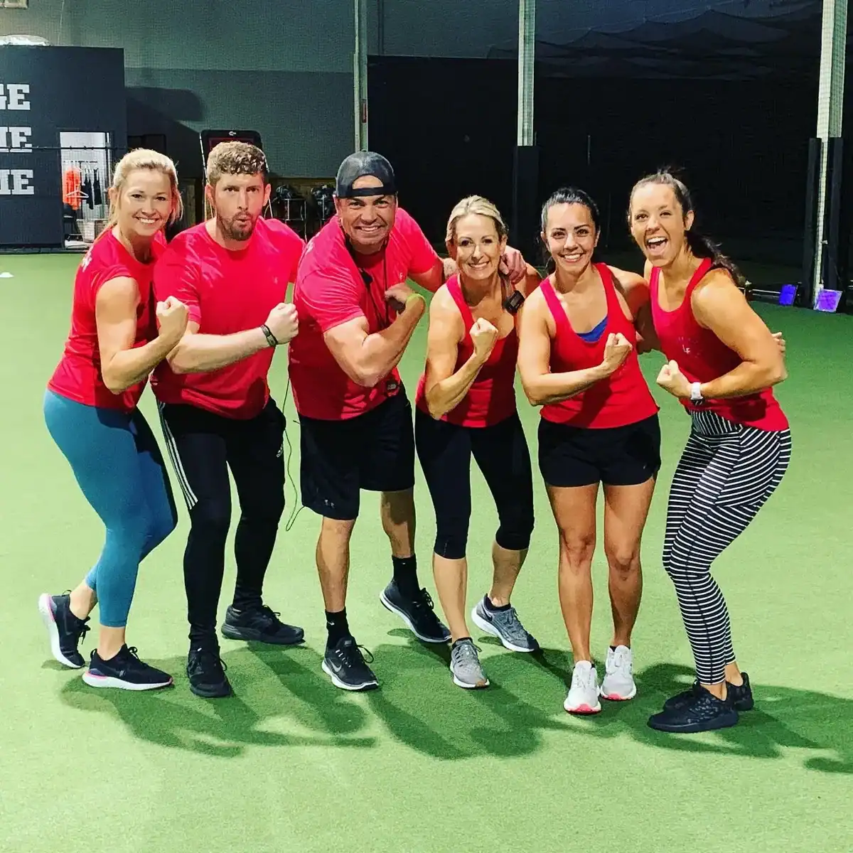 Flexing biceps, smiling in red shirts on a green gym floor.