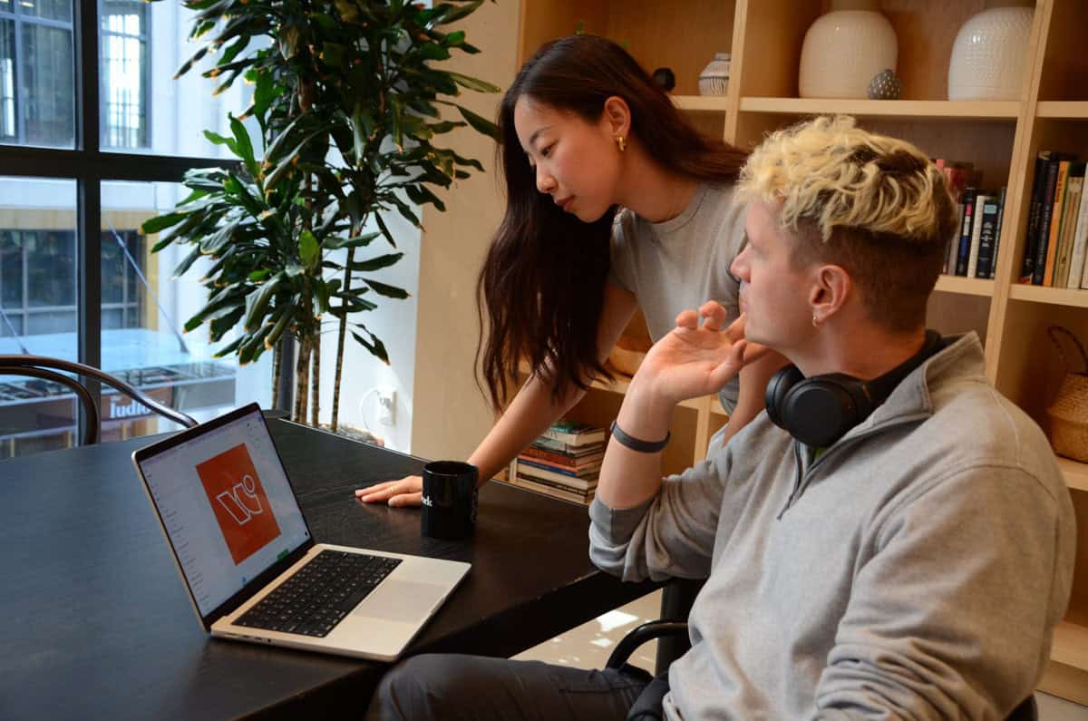 Team members collaborate on a laptop, reviewing designs in an office setting.